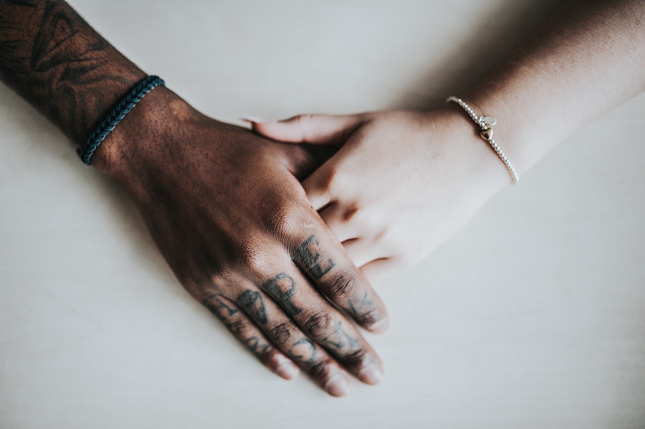 the hand of a black person with tattoos holding the hand of a white person each with bracelets
